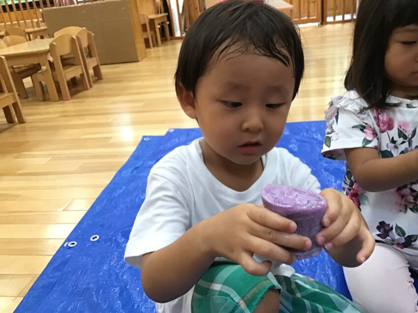 色水遊びが大好きな2歳児さん。
いつものように色水をして遊んでいると先生が「凍らせてみる？」と提案。
事務所の冷蔵庫にそーっと入れて次の日。
「うわー！アイスみたい♪固まってる！」とカチカチになった氷を触ってなんとも嬉しそうな
表情。
自分で作った氷を次は画用紙の上で滑らせて色が付くとまたまたびっくり。
スイスイ滑る氷の感触を楽しみながら自由に絵を描くことを楽しみました♪
