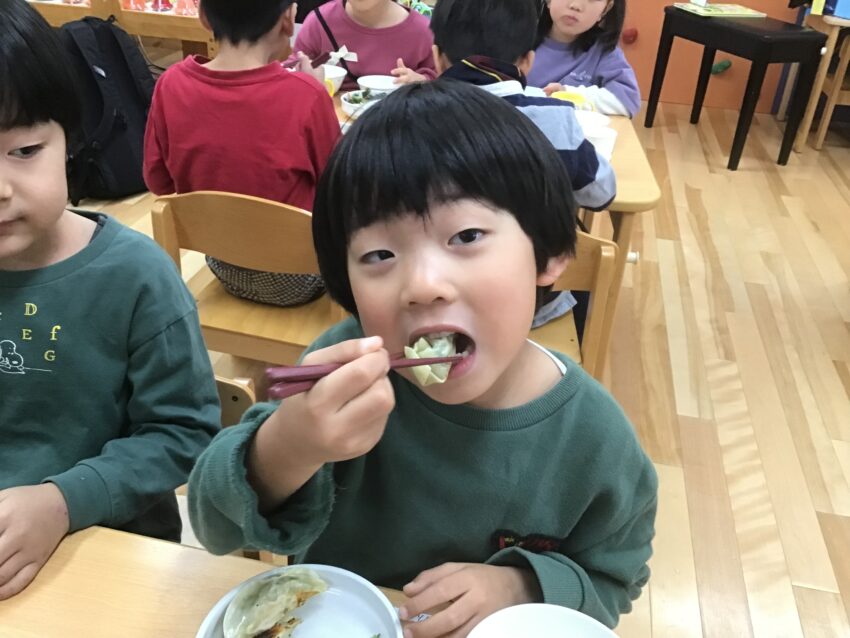 5歳児さんがみんなで餃子作りに挑戦！<br />
生姜をすりおろしたり、ニラも包丁を使って刻みました。<br />
お肉をこねるのも、とってもいい力加減で混ぜていきます。<br />
皮に包むのもみんなですると、とても楽しく出来ました♪<br />
ホットプレートに全員分並べると見応えのある餃子の数！<br />
焼き上がってくると香りが漂ってきて、食べたくて食べたくて待ちきれない様子の子どもたち。<br />
いい色に焼きあがると大喜び！！<br />
味は抜群に美味しかったです。おかわりもたくさんして、あんなにあった餃子も空になってしまいました。<br />
どの工程も指先を上手に使って出来ていたのは、小さいころから様々な玩具で指先を使って遊んでいたからですね。<br />
<br />
<br />
<br />
