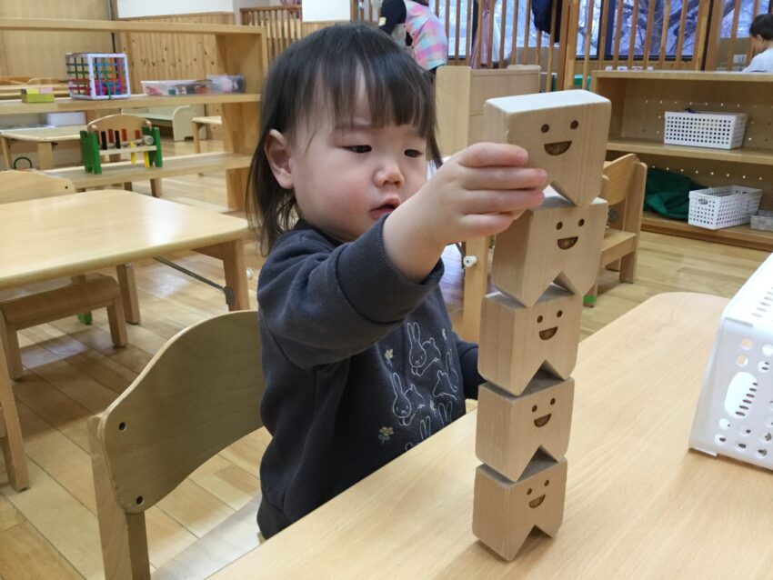 同じ積み木でも積んでみるのと並べてみるのでは形が変わっていきます。
積み木を積むときはバランス調整も必要となってきますので、集中しながら重ねていきます。
並べると積み木の顔も並んで、まるで自分に微笑みかけてもらっているようで、思わず笑顔になりました♪

