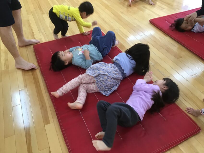 目的地に到着すると、たくさん餌をあげる真似をしました。その後はお腹が空いたのでみんなでお弁当を作りました。手を挙げて足をくっつけてマットの上を転がって美味しいウインナーを作ったり、おにぎりになりきってころんと前転をしました。
子どもたちは「鮭味にする!」「やっぱり昆布味がいい!」と一生懸命考えてなかなか列が進まないという可愛らしい姿もありました。中にはリンゴ味やクリーム味など甘いおにぎりを作った子もいて思わず笑みがこぼれてしまいました。とても楽しかったようで、始終ニコニコの子どもたちでした♪
楽しい経験から身体を動かすことも大好きになって欲しいと願っています。
