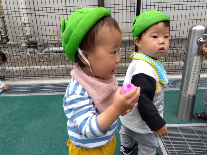 雨が降る日が多くなってきましたが、その合間を縫って１歳児さんが散歩に行きました。ボールを見つけると追いかけたり転がしたりしながら楽しんでいました。<br />
気温が上がる日も多くなってきたので、水にも触れてみる機会も作っています。小さな水風船を作って子どもたちに渡すと握った時の弾力や耳元で振った時の水の音などが楽しくていい表情になっていました。力加減が分からずに割れてしまった時は急に無くなってびっくりしていて、お友だちや濡れた指先を不思議そうに見つめていました。