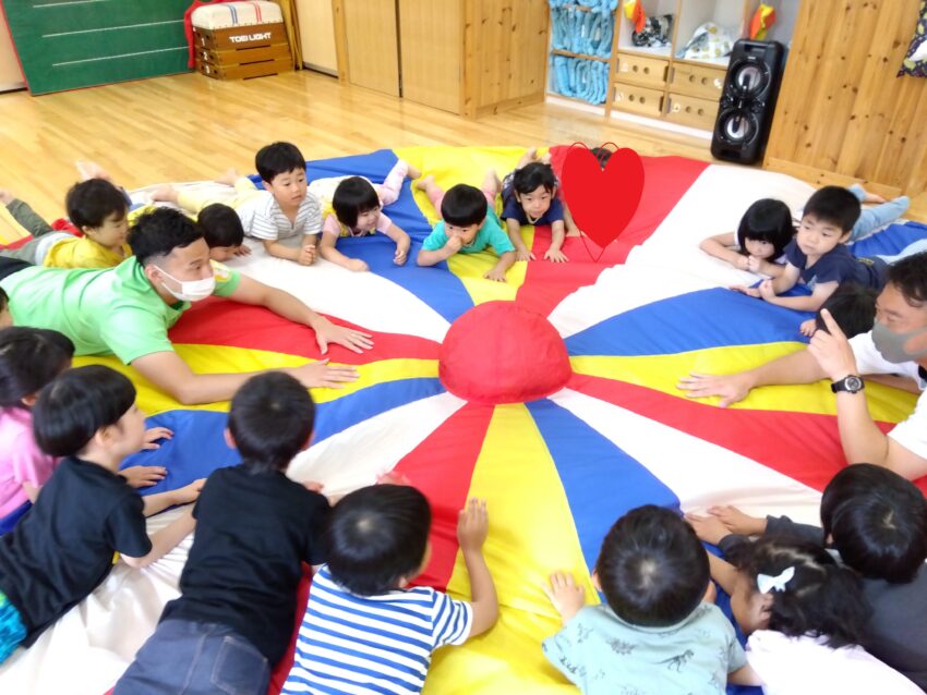 ３歳の頃からずっと憧れていた４歳児さんのパラバルーン。
体操教室の時に先生がパラバルーンを持って来ると、その様子を見た瞬間に子どもたちの目が輝き、早くやりたくてソワソワしている姿がとても可愛らしかったです。
前回行った技も覚えていて、講師の先生に聞かれると、身体を動かして表現することが出来ました。
新しい技にも挑戦して、上手く出来ると
「やったー！」「出来たね！」
と嬉しそうな子どもたち。
一人が引っ張りすぎても力が弱すぎてもバルーンはうまく膨らみません。
力加減を調整してみんなで一つのものを作り上げる経験をこれからもバルーン活動の体験を通して感じて欲しいです。