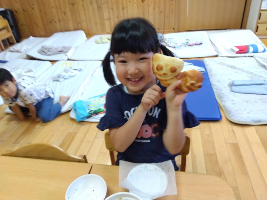 お昼寝をしている間にオーブンで焼いて出来上がった形に大喜び！
「膨らんだね～！可愛いね♪」
「イースト菌が入っているからなんだって。」
「食べるのがもったいないね～。」
と、会話をしながら自分の作ったパンをとても愛おしそうに持っていました。
ぱくっと一口食べると、とても柔らかくて思わず
「美味しい～😋」と満面の笑みが零れていました。
食べるものを自分たちで作る喜びと美味しさを感じる事が出来た子どもたちでした。