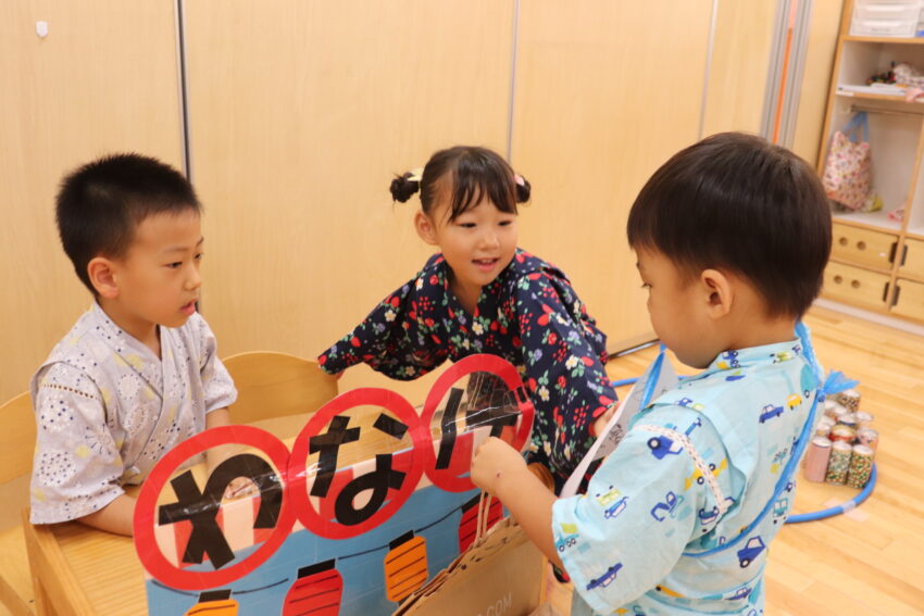 夏祭りコーナーでは5歳児さんがお店番をして案内や遊び方の説明、景品の受け渡しをしてくれます。
「いらっしゃいませ~!」
の呼びかけも威勢が良くてお客さんも嬉しそうに入っていっていました。
たくさんのお客さんで賑わってお店も大盛況!
輪投げにヨーヨー釣りに缶積み。
景品が当たると「これ、欲しかったんだ♪」
と喜びが溢れていました。
ぽけっとランド市ヶ谷保育園では様々な経験・体験をする中で自分の喜びと他者の喜びを感じられる子に育つ保育をしています😊
