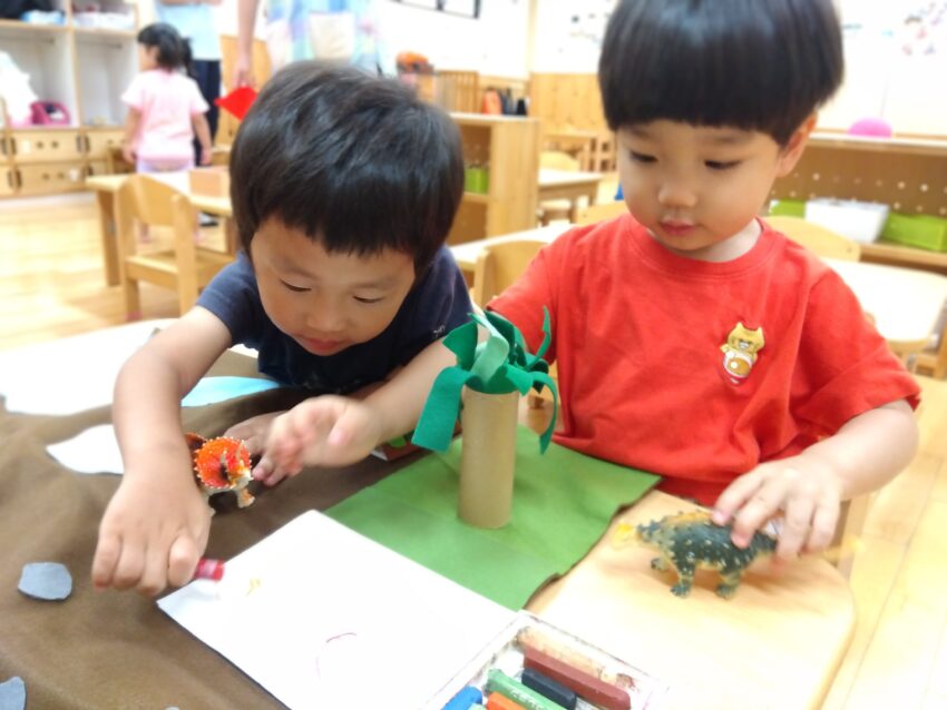 手作り玩具もたくさんあります。<br />
先生が子どもたちの好きな恐竜から遊びが発展していくように<br />
フエルトで木や岩を作ってくれました。<br />
そこから子どもたちが自分たちでも恐竜にあげたい物を描いています🖍～