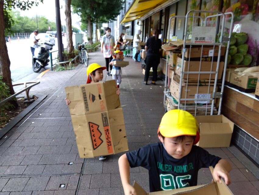 4歳児さんが自分たちが経験したお祭りを保育園でもやってみよう!ということになり、それぞれのチームでどうやって作るのかを設計図を基に話し合いました。
必要な物を考えていくうちに「ガチャガチャを作るには大きな箱が要るよね!」
という事に気づき、「じゃあ、スーパーに段ボール箱をもらいに行こう!」
と決定。