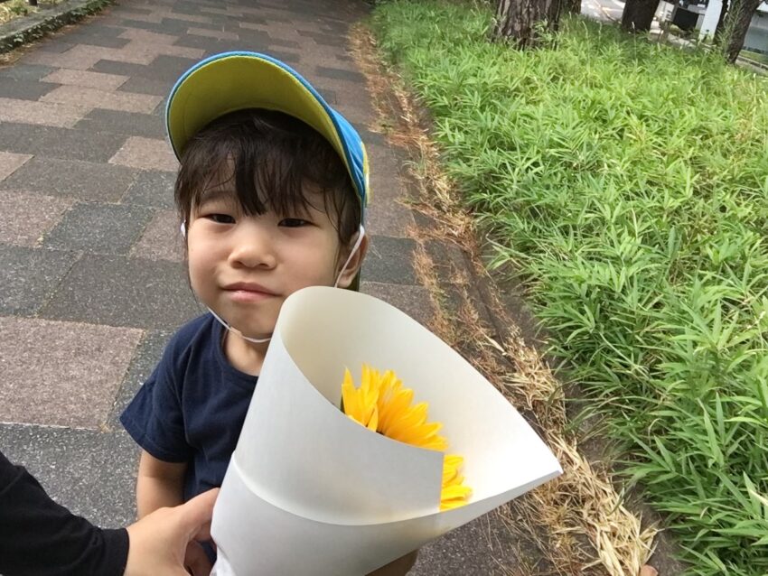 夏の花って何だろう?
先生と3歳児さんが考えて「やっぱりひまわりじゃない?」という事になり、
ひまわりのお花を花屋さんまでお買い物に行きました。
花屋さんに着くと保育者の真似をして「おはようございます!」
と元気いっぱいに挨拶をすることが出来ました。
買った後も「ありがとうございました!」「さようなら。」
と挨拶をすることができ、挨拶を返してもらった事や褒められた事を喜びに感じていました。
市ヶ谷保育園では地域の方に接する際に自分から挨拶が出来るように、相手の思いや気持ちを考えながら挨拶の大切さを子どもたちに伝えています。