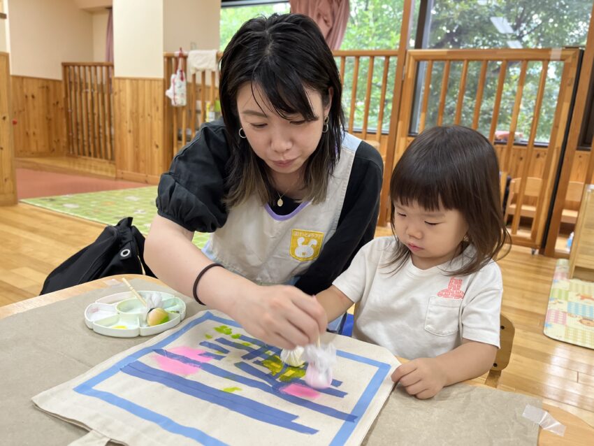 テープを貼った後は絵の具をポンポンしながら色付けをしていきます。
色が重なっていく面白さとポンポンする楽しさを保護者の方と一緒にしていきます。
お母さんやお父さんとすることでいつも以上に楽しそうな子どもたち😊
