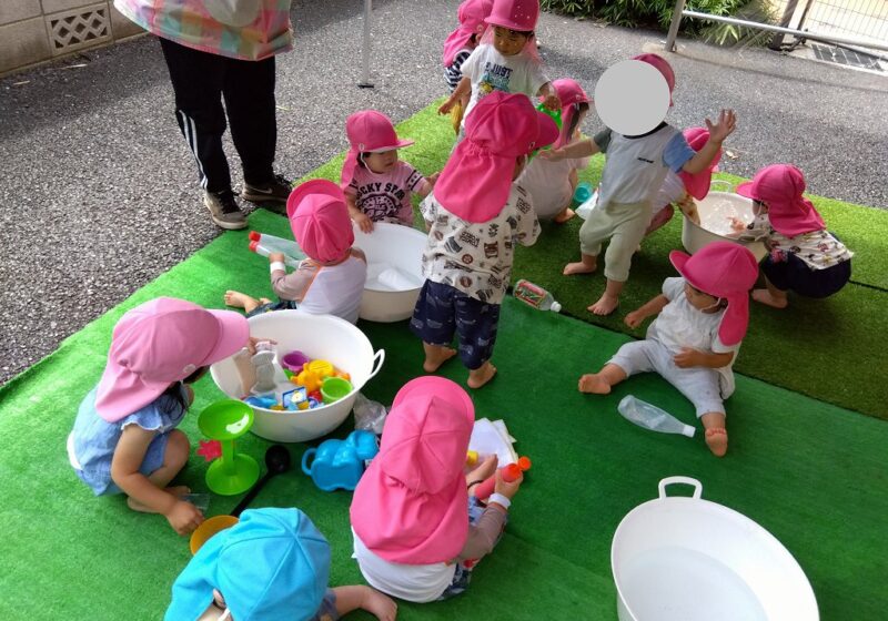 待ちに待った水遊びが始まりました！おもちゃやカップを手に取ってタライの中の水をすくって遊ぶ子どもたち。
